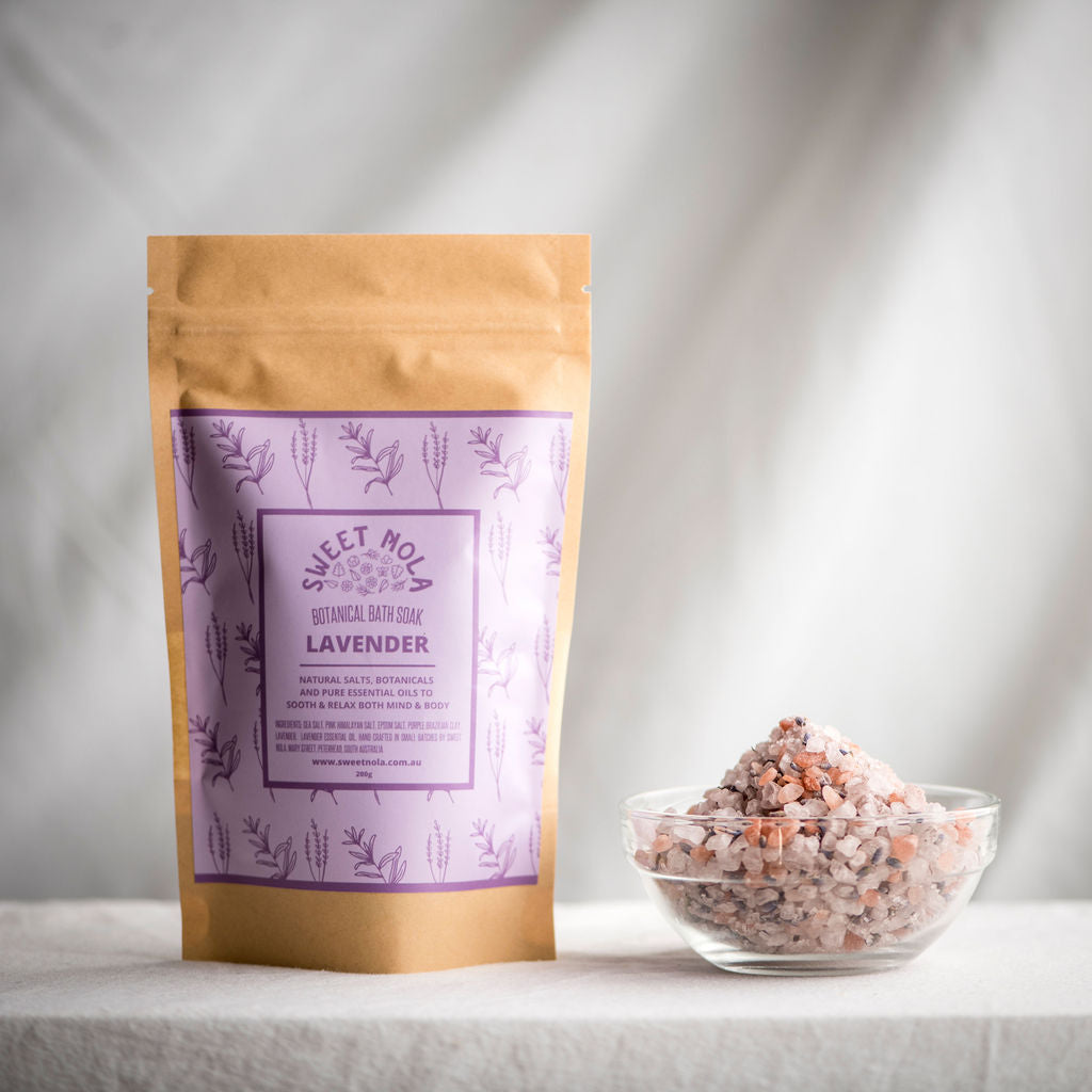 Lavender Bath soak in paper stand up pouch with purple label. On the right is a small glass bowl filled with the bath soak salts.